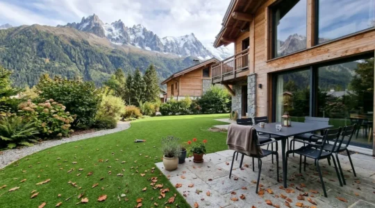 Jardin impeccable d'une résidence secondaire avec gazon verdoyant et terrasse aménagée en arrière-plan montagneux